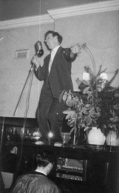 Old photo of man standing on piano and singing